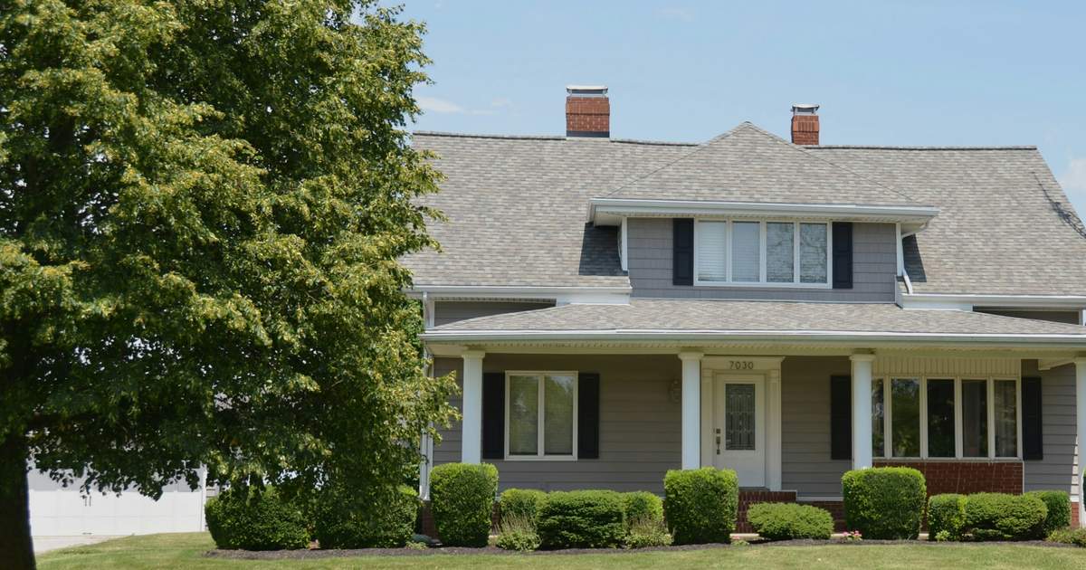 A gray two-story family home with a white columned porch and a green front lawn
